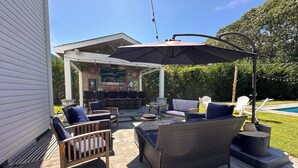 Un patio al aire libre con muebles de mimbre, una zona de estar cubierta y una piscina al fondo.