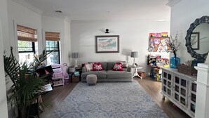 Un salón amplio con un sofá gris, alfombra estampada y una estantería llena de libros y objetos decorativos.