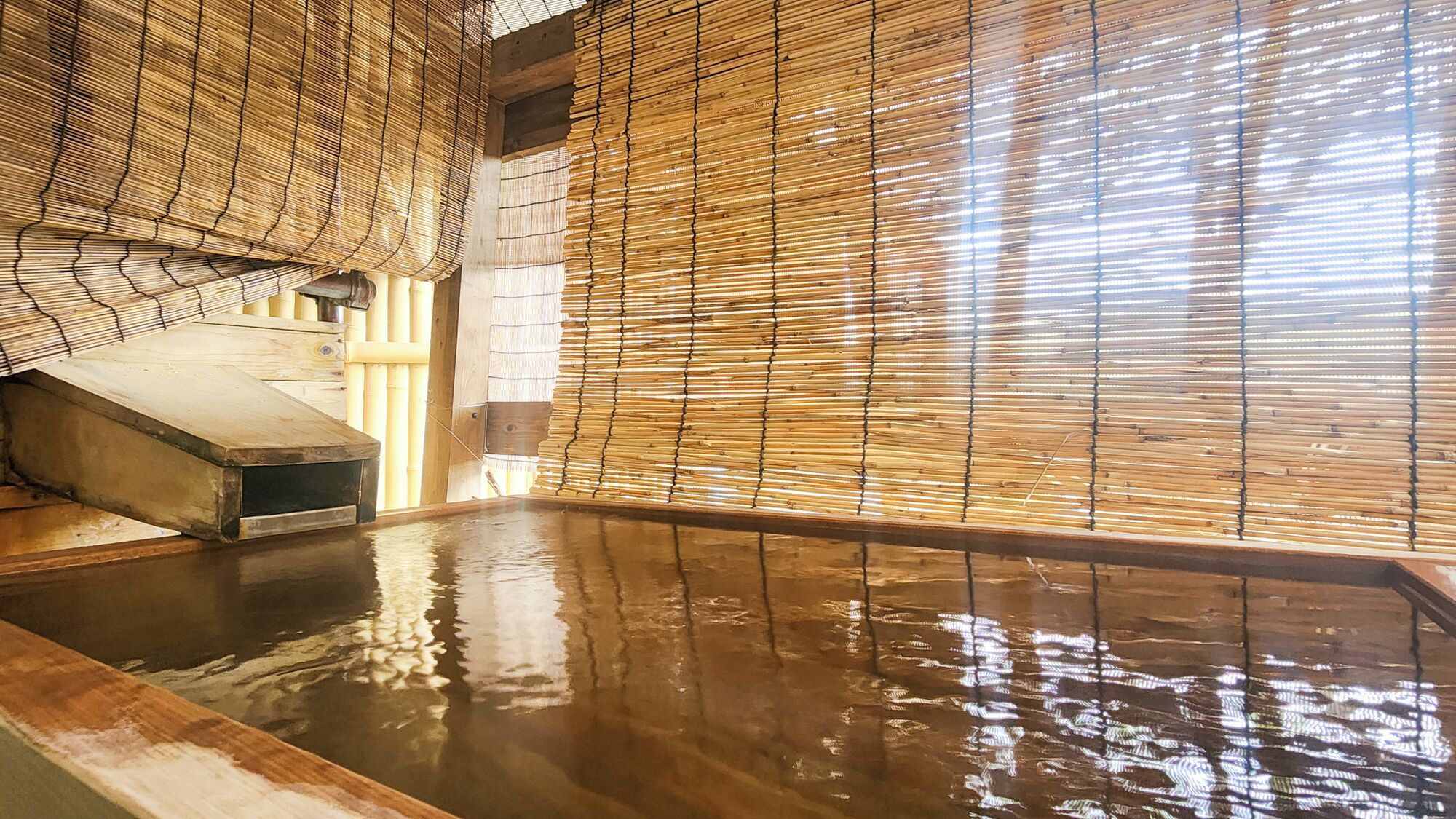 A traditional Japanese onsen with a wooden interior, a hot spring bath, and a wooden bench.