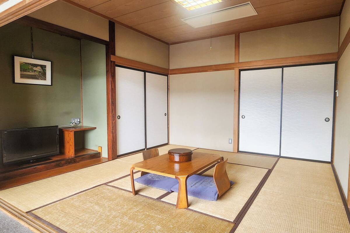 A traditional Japanese room with tatami flooring, a low wooden table, a television, and sliding doors.