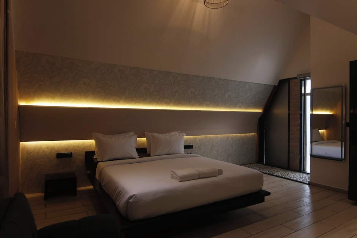 Une chambre d’hôtel moderne avec un grand lit, des tables de chevet, un miroir et une banquette intégrée.