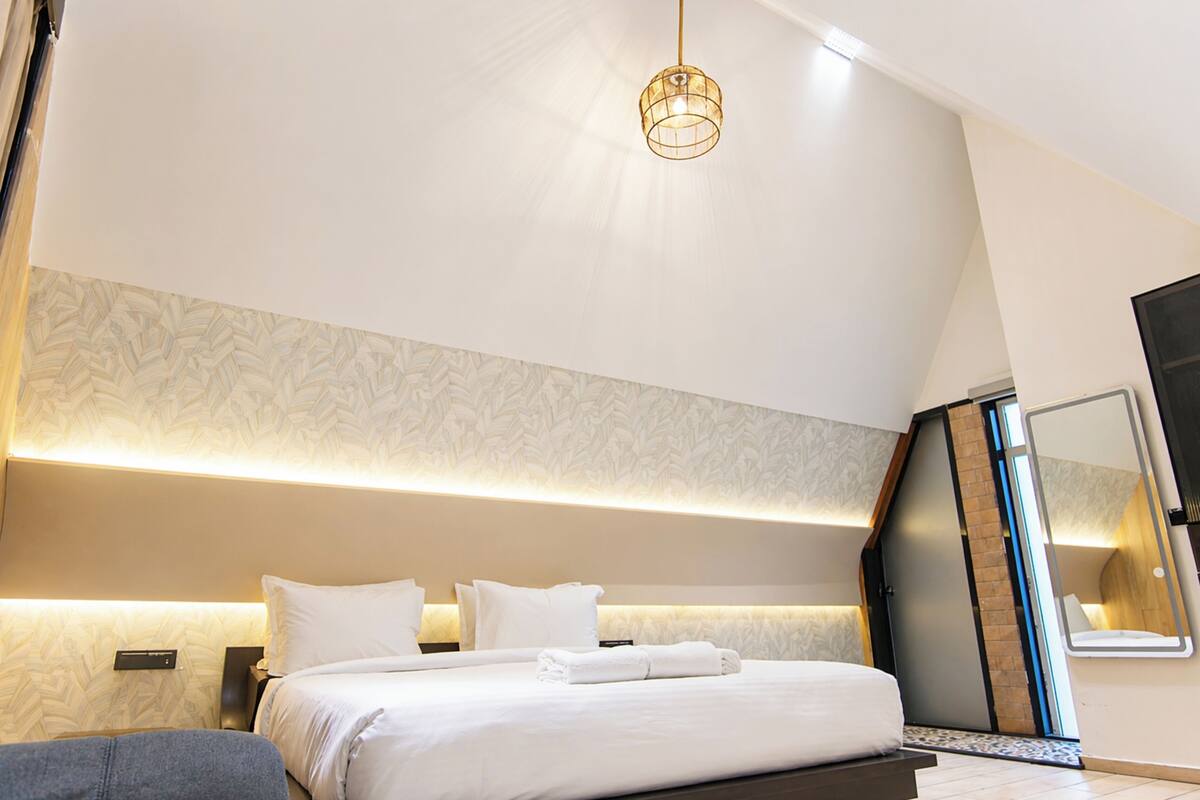 Une chambre d’hôtel moderne avec un grand lit, une table de chevet, une petite table, une lampe fixée au mur et un miroir.