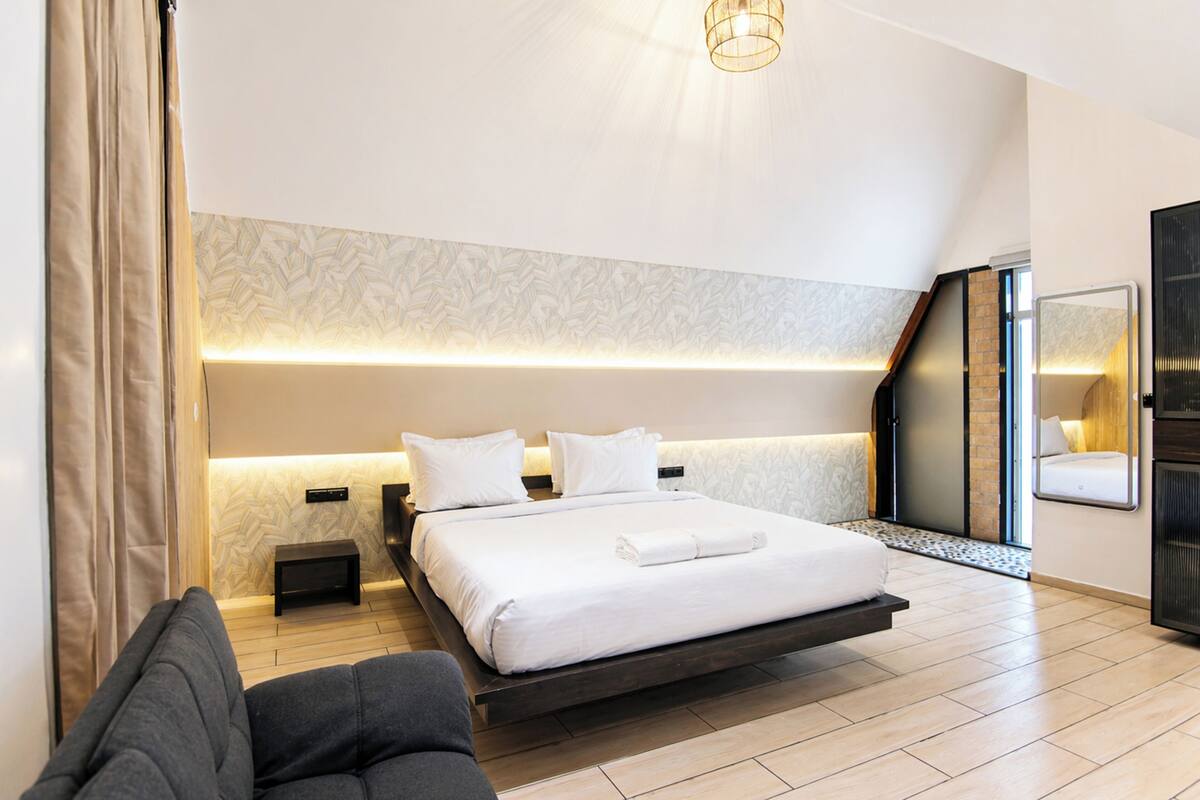 Une chambre d’hôtel moderne équipée d’un lit, d’un canapé, d’une petite table et d’un miroir.
