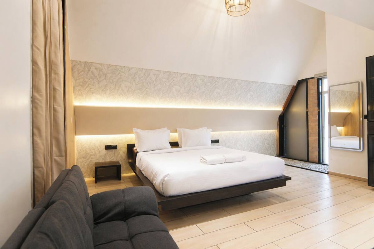 Une chambre à coucher moderne avec un lit, des tables de chevet, un banc et un grand miroir.