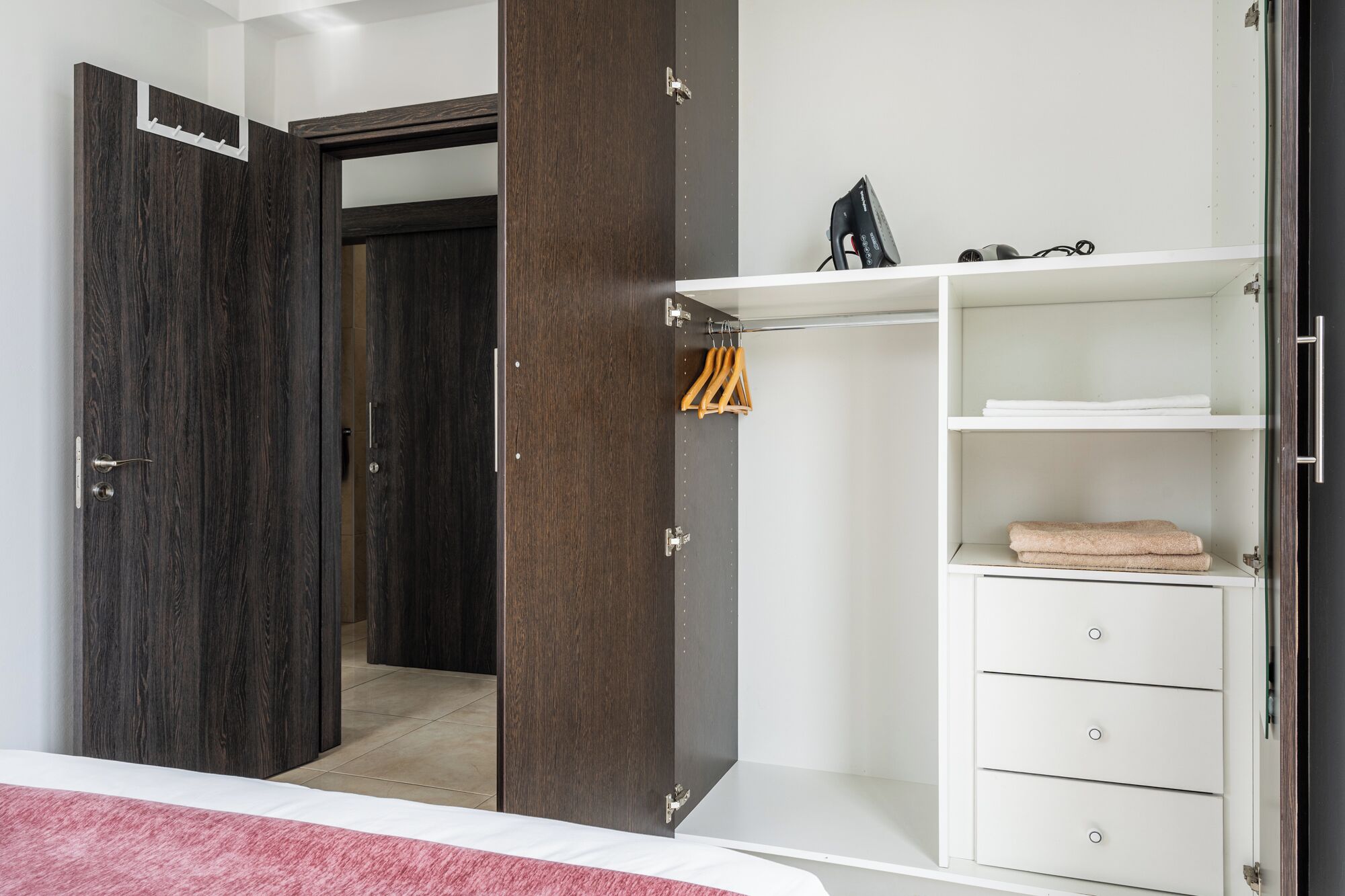 A bedroom with a wardrobe, a bed, and a bathroom visible through an open door.