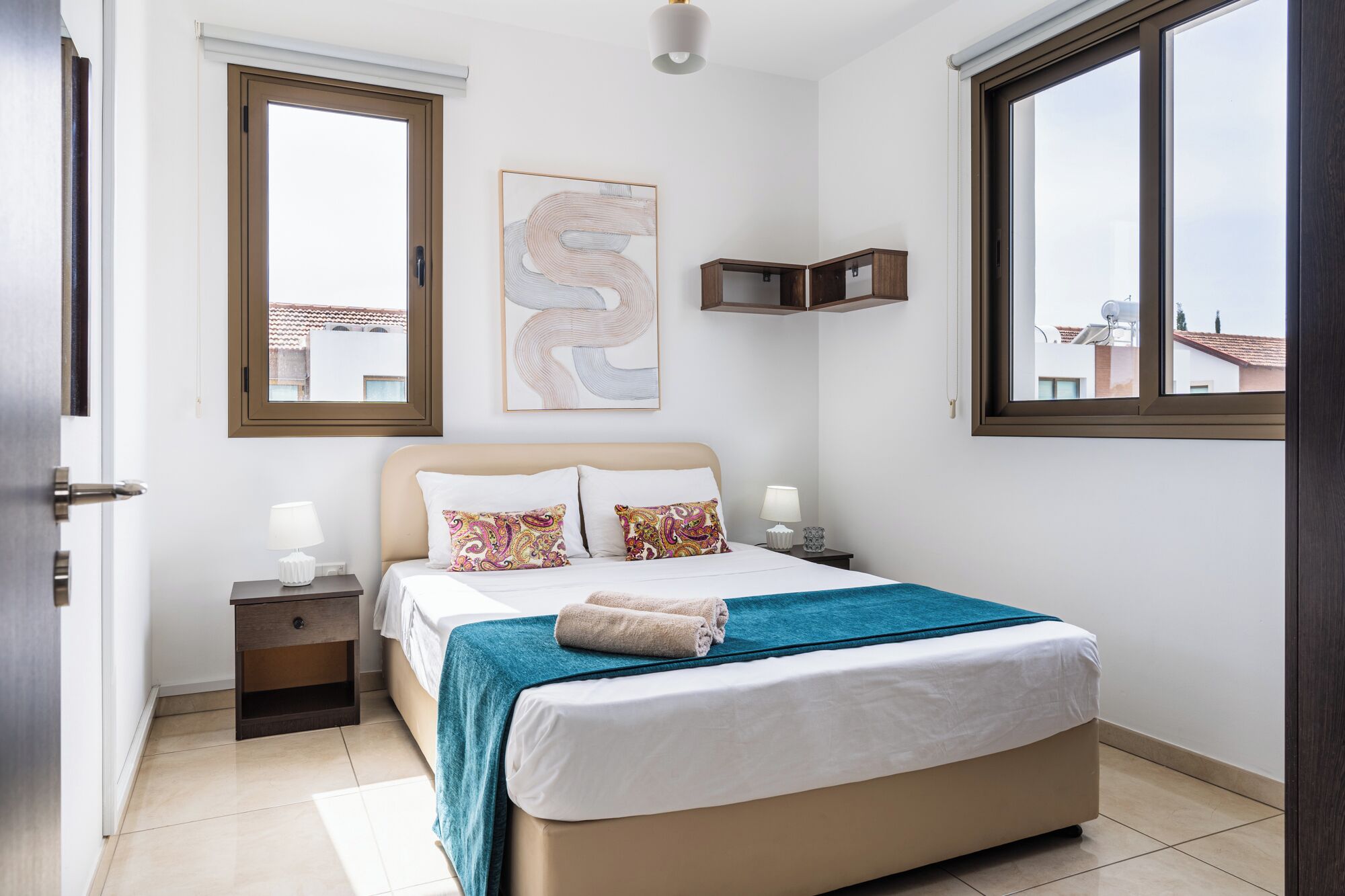 Un dormitorio con cama, mesitas de noche, una ventana y una obra de arte en la pared.