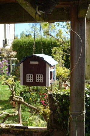 A birdhouse hanging outdoors, surrounded by greenery and a stone wall. - House with river access and sauna at the foot of the château, La Flèche zoo and 24h (Durtal)