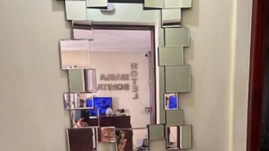 Un interior moderno con una consola de vidrio, un jarrón decorativo con flores azules y un espejo con varios espejos más pequeños.
