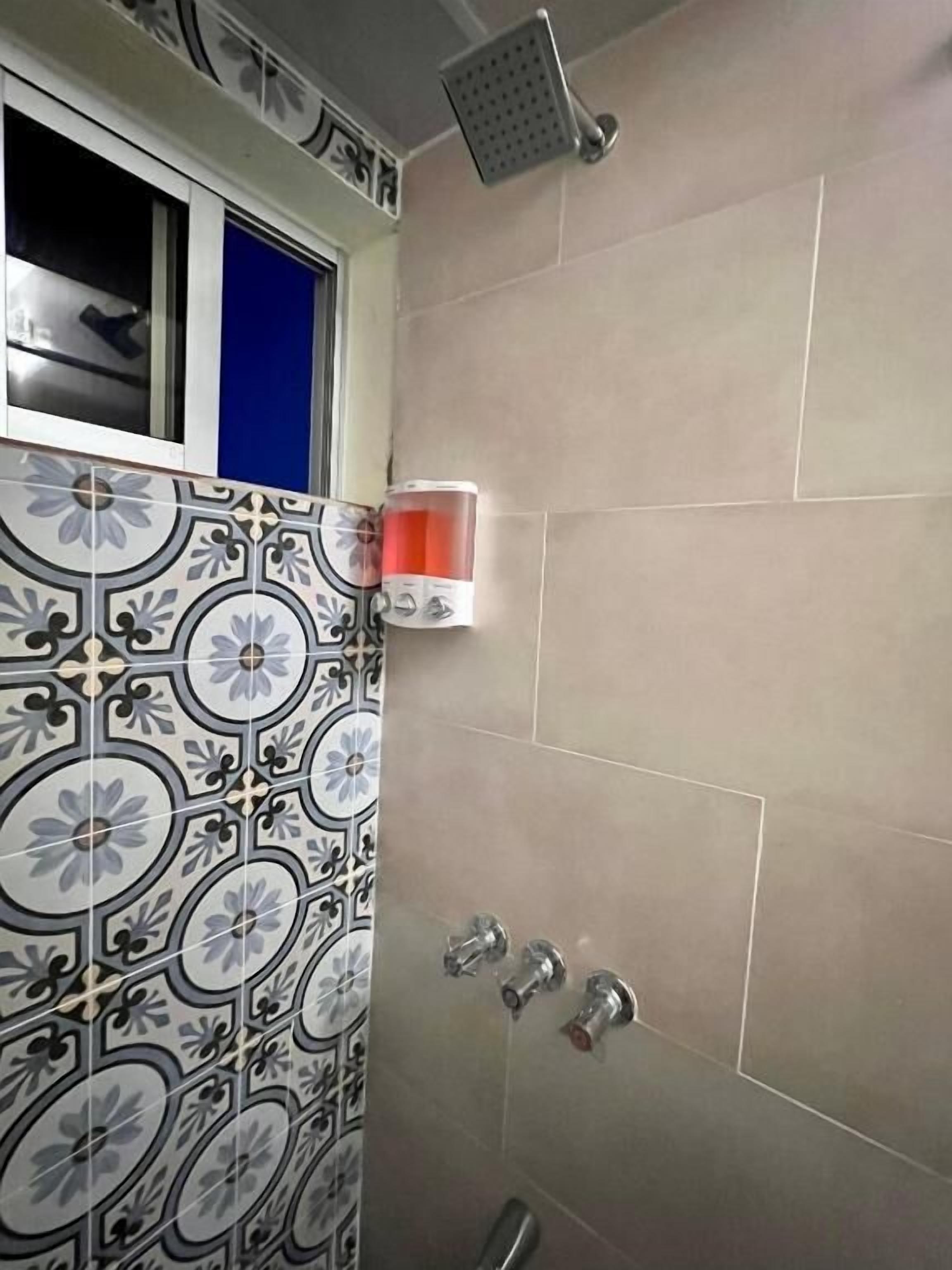 A bathroom with patterned tiles, a showerhead, and a window.