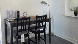 A room with a dark wooden dining table, two chairs, a lamp, a small potted plant, and a window with a mirror.