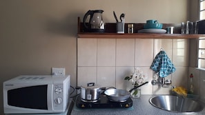 Una cocina con microondas, estufa, ollas, un lavamanos y una ventana con luz natural.