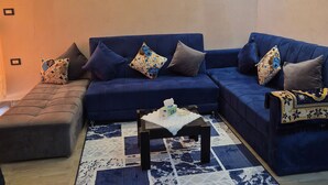 A living room with a blue sofa set, a coffee table, patterned rug, wall-mounted lights, and a decorative vase painting. - Star Apartment 2 Hurghada (Hurghada)