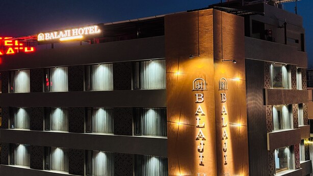 Et hotel med en moderne facade, flere balkoner og oplyst skiltning.
