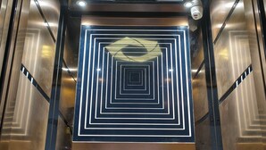 Elevatorinteriør med metalliske vægge og geometriske lysmønstre.