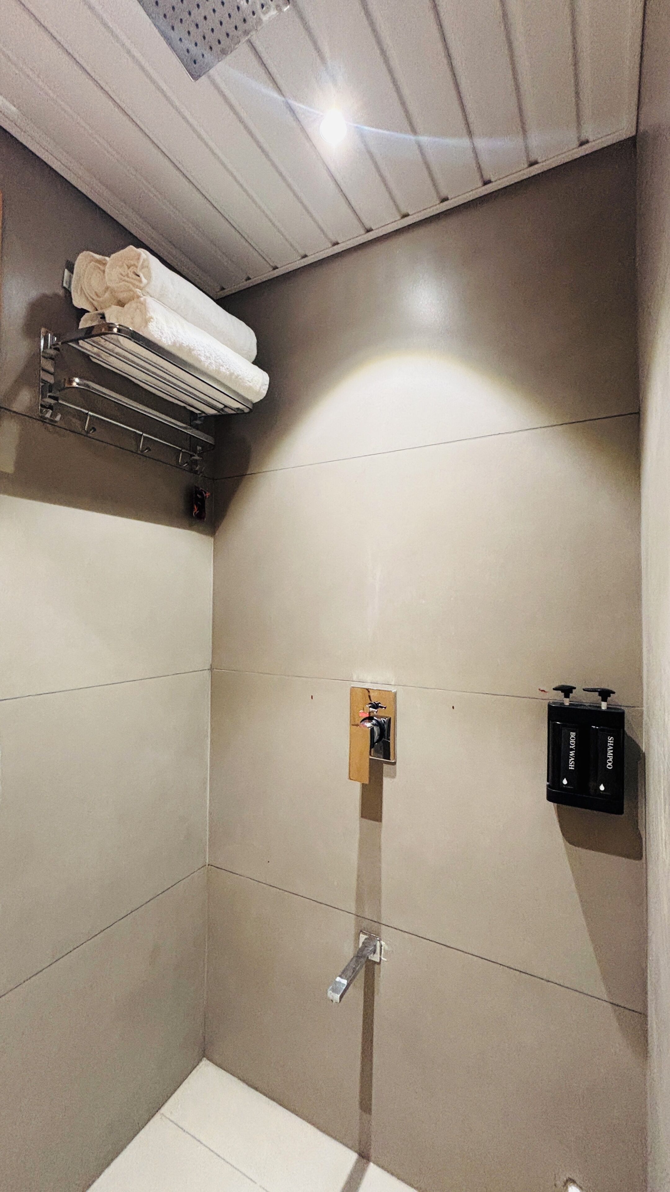 A modern bathroom with a shower, a towel rack, and a soap dispenser.
