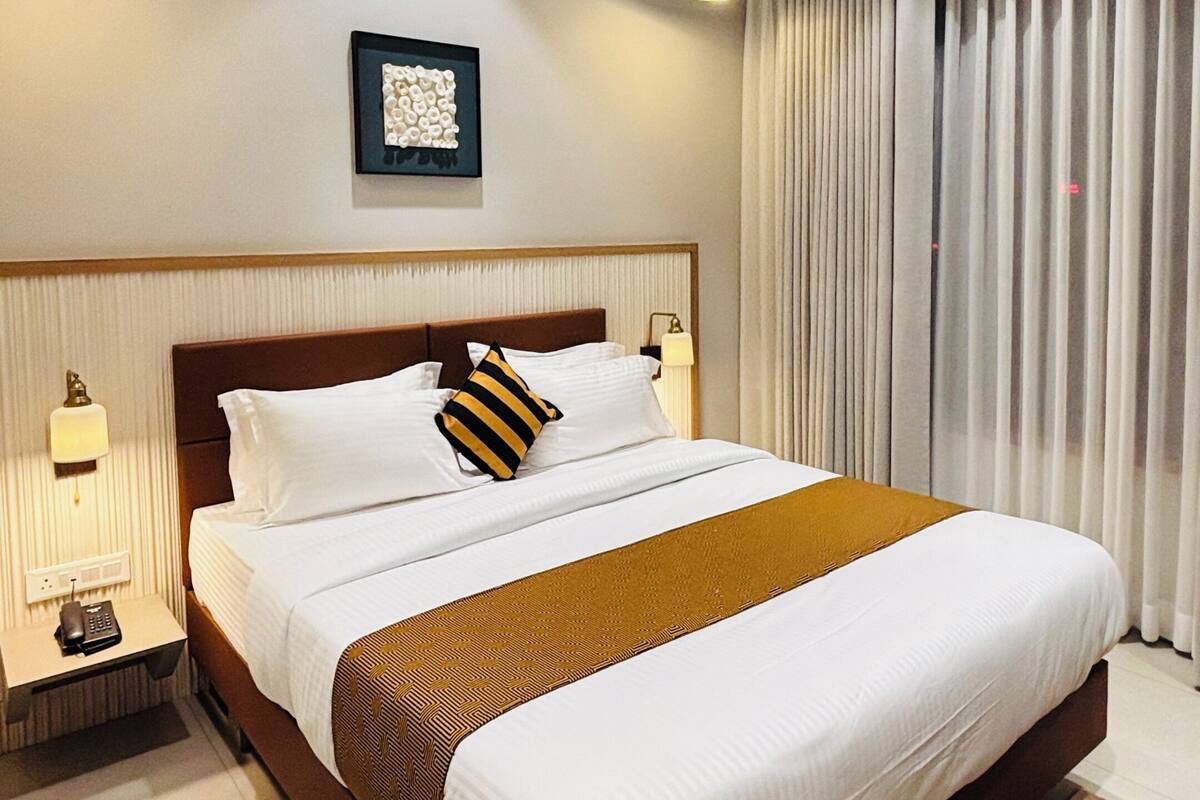 Ein modernes Hotelzimmer mit einem großen Bett, Nachttischlampen, einem gerahmten Kunstwerk an der Wand und Blick durch Vorhänge nach draußen.