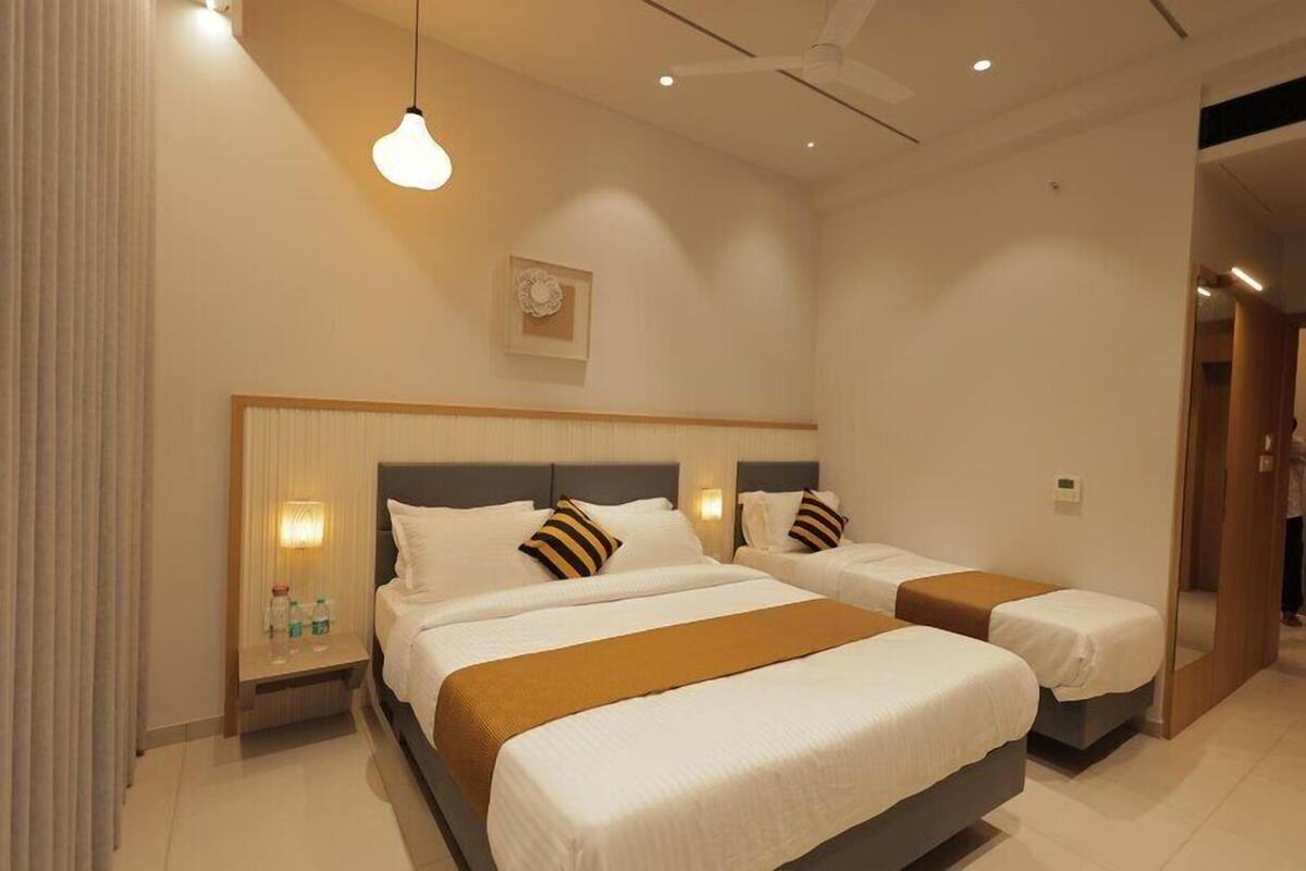 Ein Hotelzimmer mit zwei Betten, einem Nachttisch mit Lampe, einer Wanduhr und einem Deckenventilator.