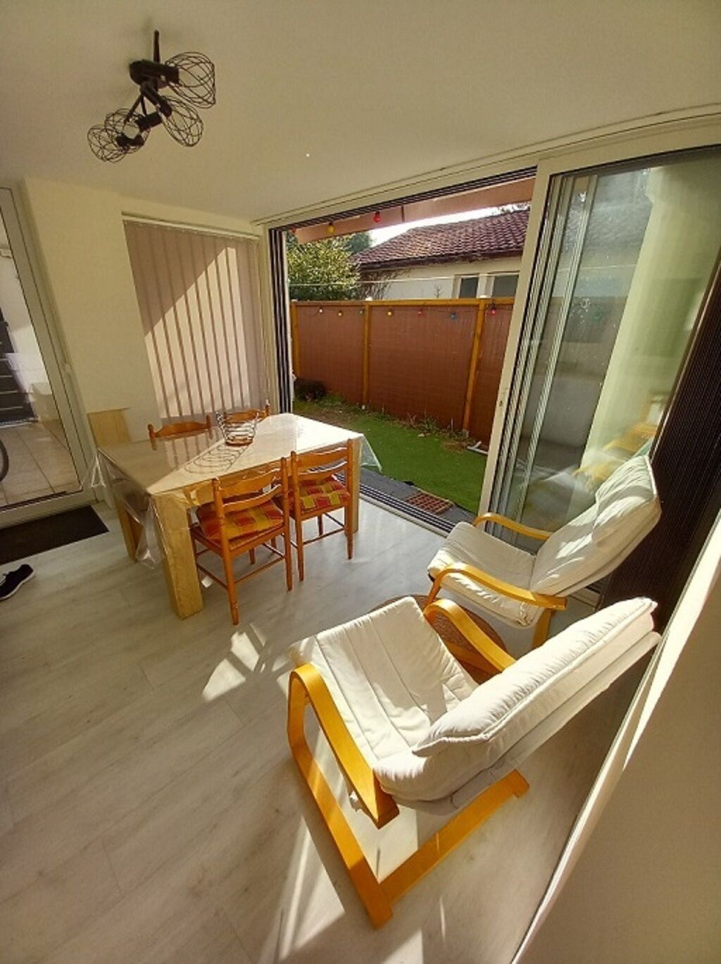 A patio with a table and chairs, a sliding glass door leading to a garden, and a ceiling fan.