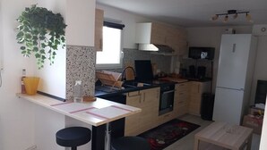 Kompakti keittiö, jossa on keskeinen saareke, baarituoleja, pieni ruokapöytä ja jääkaappi.