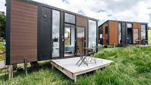 A modern, two-story house with large glass windows, a wooden deck, and outdoor furniture.