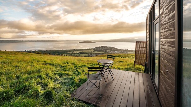 A wooden deck with a table and chairs overlooking a scenic landscape with a body of water and distant hills.