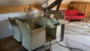 Un coin repas avec une table et des chaises en verre, un canapé rouge et des poutres en bois.