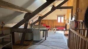 Une pièce de style « loft » avec des poutres en bois apparentes, un lit en mezzanine, un bureau et une chaise rouge.