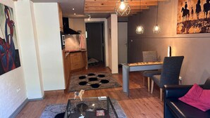 Een woonkamer met een glazen salontafel, een bank, een eettafel met stoelen, en een keuken op de achtergrond.