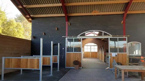 Een overdekte buitenruimte met een betegelde vloer, houten banken en een metalen poort.