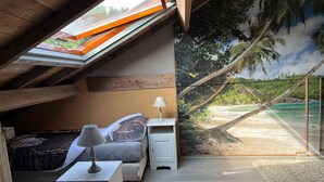 Een zolderkamer met schuine wanden, een bed, nachtkastjes, een lamp en een muurschildering van een strand.