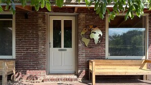 Een bakstenen gebouw met een witte deur, een bankje en een raam met uitzicht.
