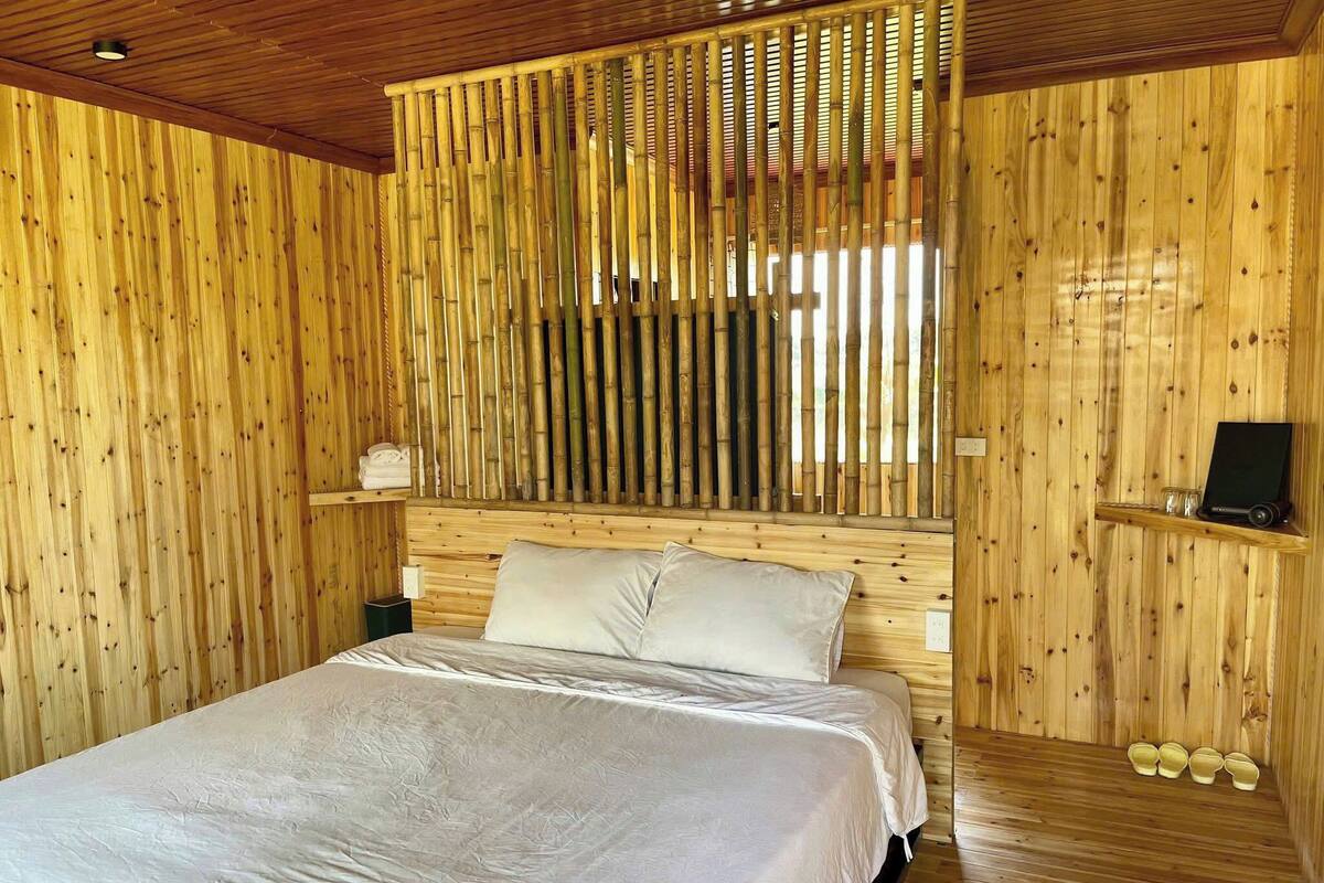 Une pièce en bois avec un lit, une étagère sur laquelle se trouve un haut-parleur et un paravent en bambou.