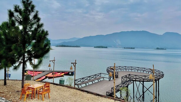 A lakeside view with a wooden dock, a table with chairs, and a large tree. - The L'anmien Bui Vien (Ho Chi Minh City)