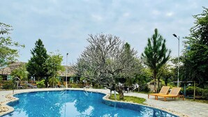 A swimming pool with a curved edge, surrounded by trees and a lounge area with chairs. - The L'anmien Bui Vien (Ho Chi Minh City)