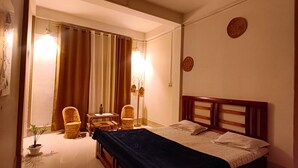 A hotel room with a bed, two chairs, a small table, a lamp, and a ceiling fan.