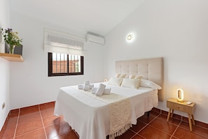 Quarto com cama, mesa de cabeceira e janela com persianas.
