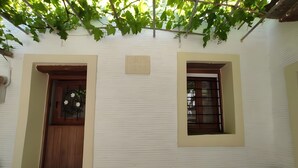 A white building with a wooden door and window, a small porch with cushions, and a sign above the door. - Country House 'Ktima Kariofillis' with Mountain View and Private Terrace (Révmata)