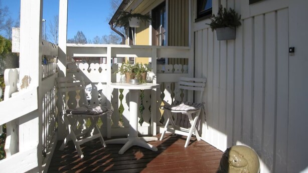 A covered outdoor area with white railings, a table with chairs, and a potted plant.