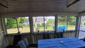 Eine überdachte Terrasse mit Tisch und Stühlen, großen Fenstern und Blick auf den Garten.