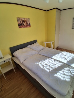 Ein Zimmer mit einem Bett, einem Nachttisch, einem Wandbild und einer Tür.