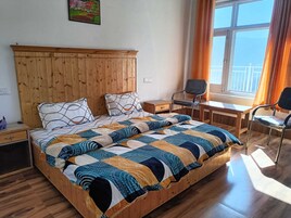 A bedroom with a wooden headboard, a bed with patterned bedding, a desk, two chairs, and a window with curtains.