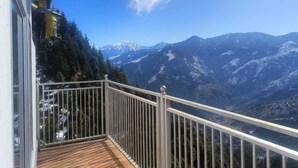 A balcony with a view of snow-capped mountains and a building with yellow accents. - Hotel Satya (Chamba)