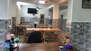 A dining area with multiple wooden tables and chairs, a ceiling fan, a flat-screen TV, and stone-patterned walls. - Hotel Satya (Chamba)