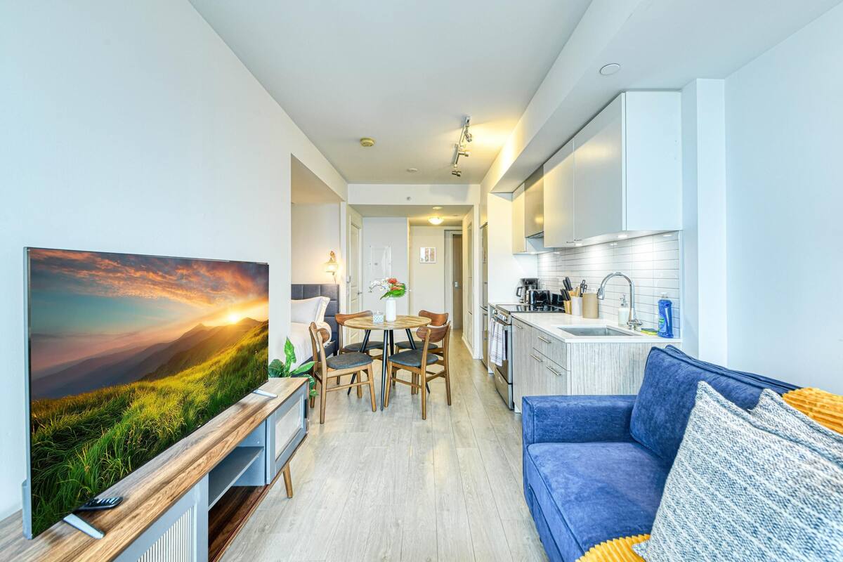 Una sala moderna con un televisor de pantalla plana grande, un sofá azul y una zona de comedor con muebles de madera.
