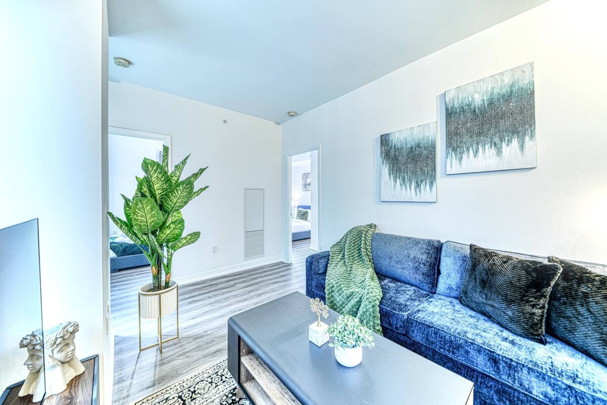 Una sala de estar moderna con un sofá azul, una mesa de centro, una planta verde grande y obras de arte en la pared.