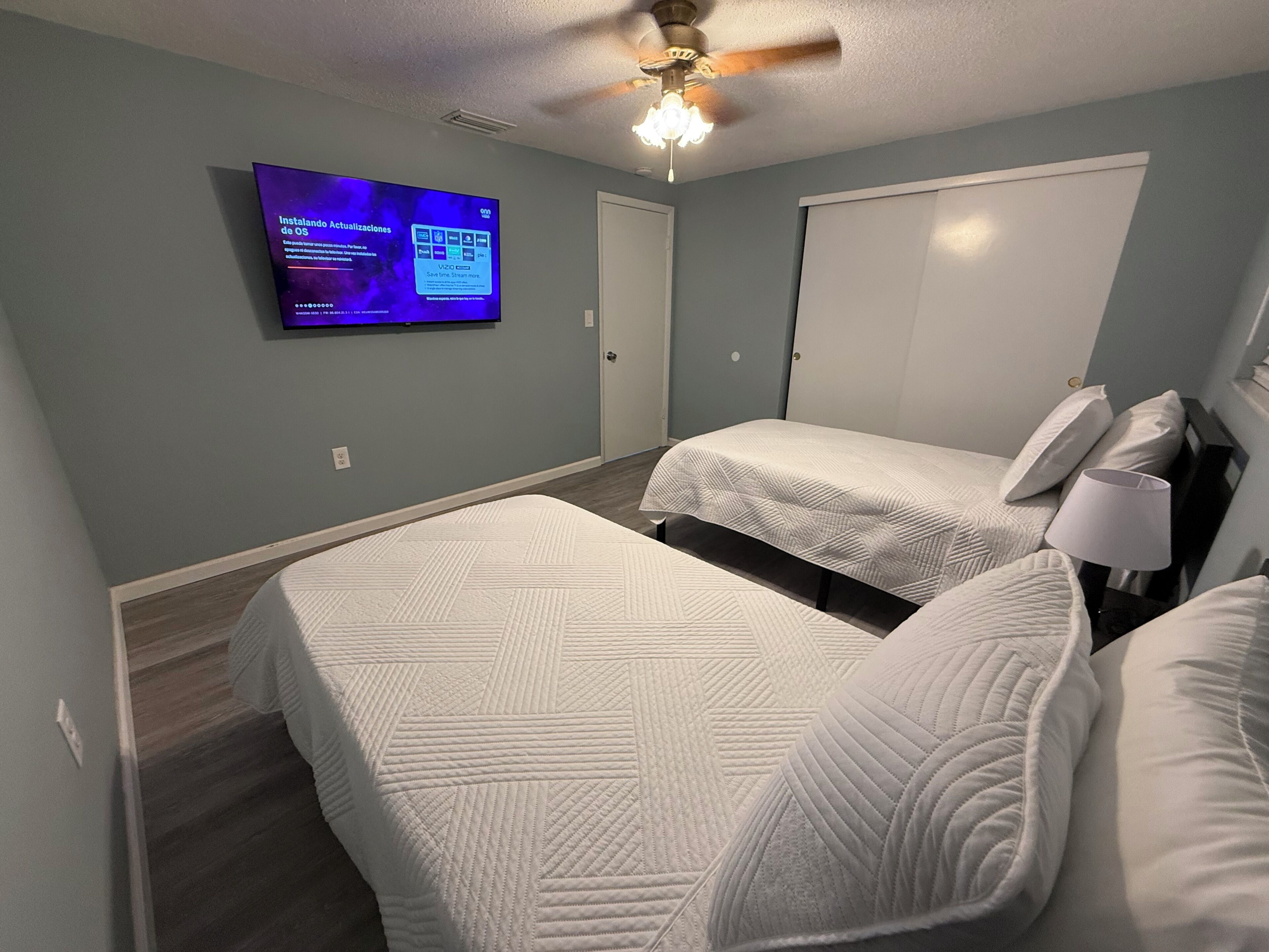 A bedroom with two beds, a ceiling fan, and a TV mounted on the wall.
