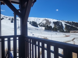 Paisagem montanhosa coberta de neve, com um teleférico e uma estrutura de madeira ao primeiro plano.