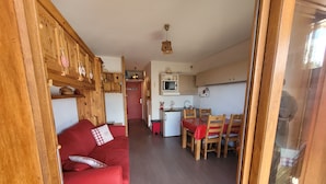 A compact living space with a red sofa, wooden furniture, a kitchen area, and a dining table. - Cosy apartment, superb view at the foot of the slopes. (Selonnet)