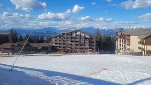 A snow-covered ski slope with a building featuring multiple balconies and a mountain backdrop. - Cosy apartment, superb view at the foot of the slopes. (Selonnet)