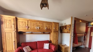 A red sofa with heart-patterned pillows, wooden cabinets with heart-shaped decorations, and a bunk bed with red curtains. - Cosy apartment, superb view at the foot of the slopes. (Selonnet)